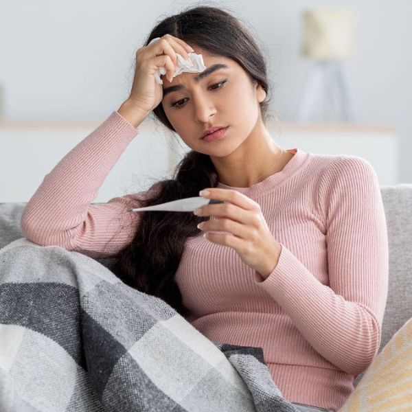 A sick woman on the couch checking her fever